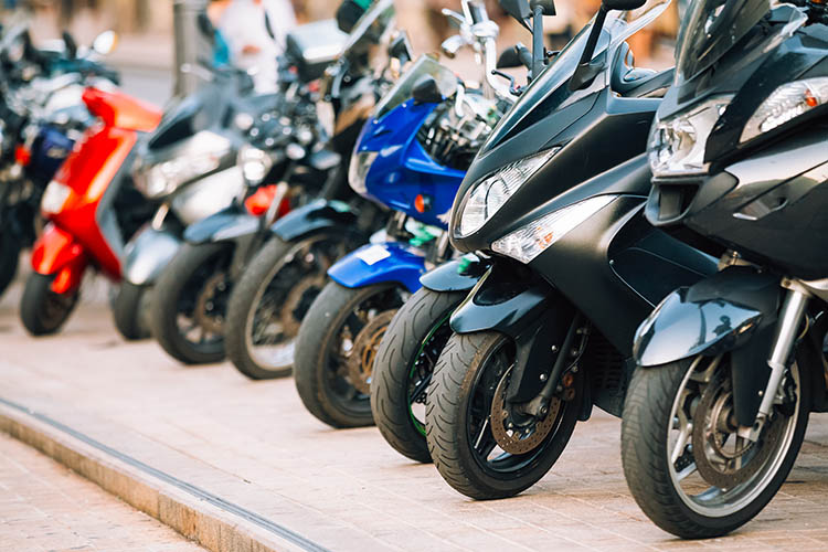 Motos i escúters aparcats en fila al carrer de la ciutat. Primer pla d'una roda